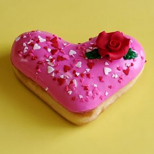 A beautifully decorated Valentine’s Pink Rose Heart Donut, coated in smooth pink icing, sprinkled with heart-shaped sprinkles, gold star accents, and edible gold sprinkles, and topped with a delicate candy rose. A perfect romantic treat for Valentine’s Day.