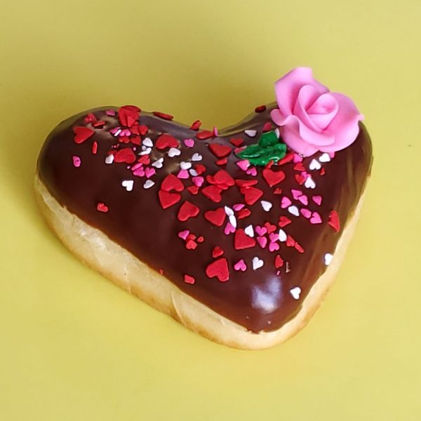 A beautifully decorated Valentine’s Chocolate Rose Heart Donut, coated in smooth chocolate icing, sprinkled with gold star sprinkles, heart-shaped decorations, and edible gold accents, and topped with a delicate candy rose. A perfect romantic treat for Valentine’s Day