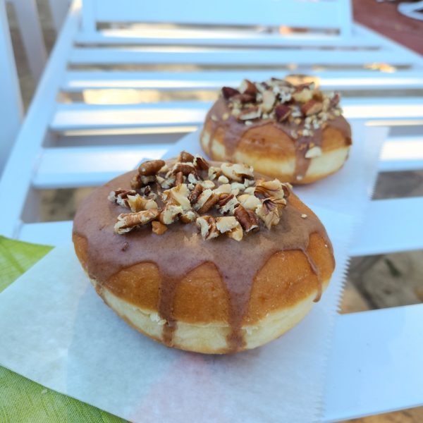 A Thanksgiving donut with a round éclair shape, filled with purple yam jam, topped with a cinnamon glaze and a mix of chopped nuts.