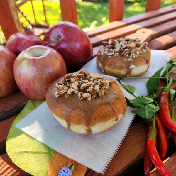 A Thanksgiving donut with a round éclair shape, filled with purple yam jam, topped with a cinnamon glaze and a mix of chopped nuts.