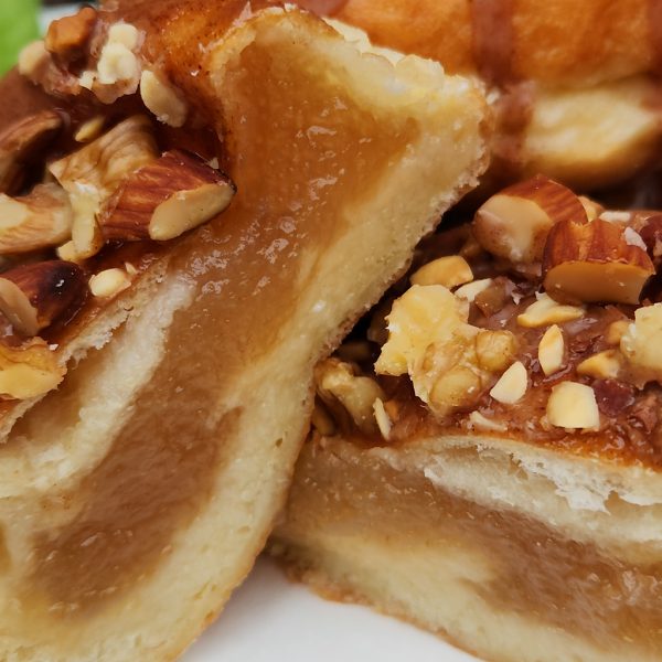 A Thanksgiving donut with a round éclair shape, filled with purple yam jam, topped with a cinnamon glaze and a mix of chopped nuts.