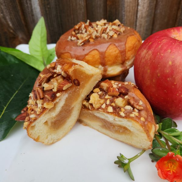 A Thanksgiving donut with a round éclair shape, filled with purple yam jam, topped with a cinnamon glaze and a mix of chopped nuts