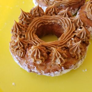 A crispy donut made from small dough pieces joined together, topped with a smooth swirl of cookie butter. The donut has a unique, textured appearance and is coated in powdered sugar.