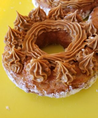 A crispy donut made from small dough pieces joined together, topped with a smooth swirl of cookie butter. The donut has a unique, textured appearance and is coated in powdered sugar.