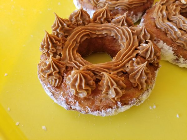 A crispy donut made from small dough pieces joined together, topped with a smooth swirl of cookie butter. The donut has a unique, textured appearance and is coated in powdered sugar.