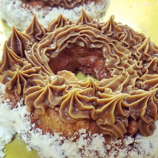 A crispy donut made from small dough pieces joined together, topped with a smooth swirl of cookie butter. The donut has a unique, textured appearance and is coated in powdered sugar.