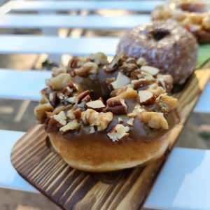 A Thanksgiving donut with a maple icing glaze, topped with a mix of chopped pecans, walnuts, and almonds. The donut is fluffy and crunchy nut topping that adds texture and flavor. Perfect for the holiday season.