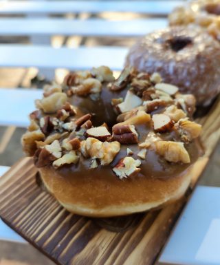 A Thanksgiving donut with a maple icing glaze, topped with a mix of chopped pecans, walnuts, and almonds. The donut is fluffy and crunchy nut topping that adds texture and flavor. Perfect for the holiday season.