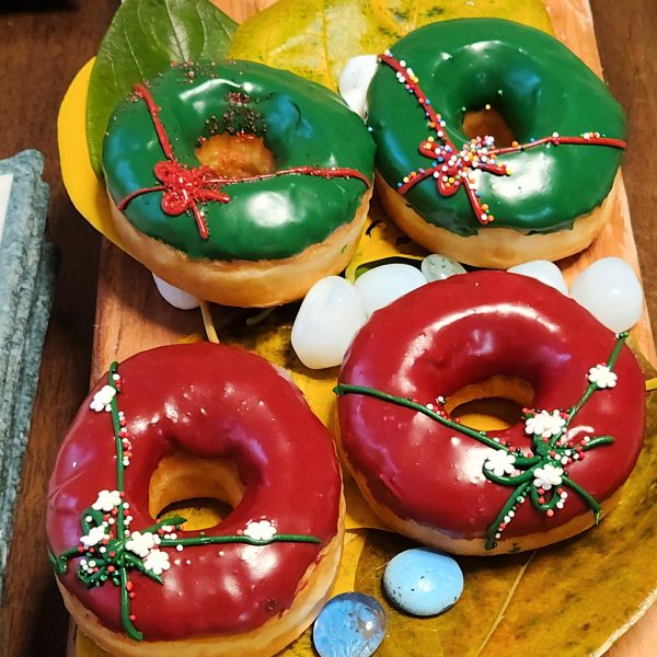 A Christmas-themed donut with green or red icing, decorated with red or green ribbon details and colorful sprinkles, perfect for holiday celebrations.