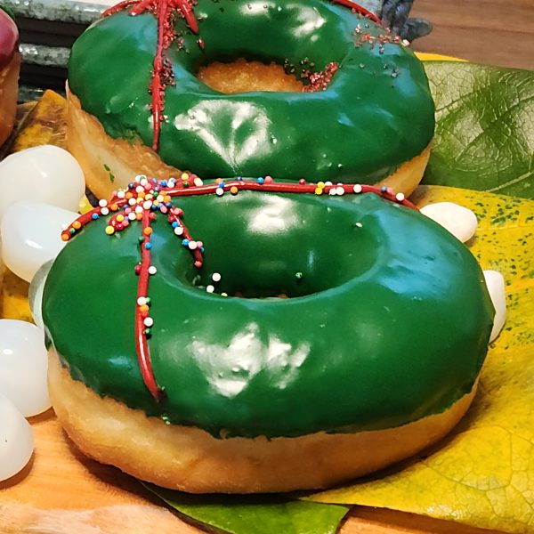 A Christmas-themed donut with green icing, decorated with red ribbon details and colorful sprinkles, perfect for holiday celebrations.