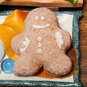 A gingerbread man-shaped donut, coated in sugar glaze, filled with spiced ginger cream cheese, and decorated with icing details, perfect for Christmas celebrations.