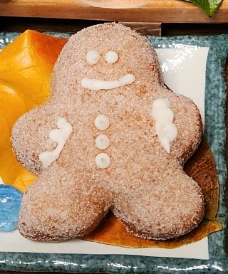 A gingerbread man-shaped donut, coated in sugar glaze, filled with spiced ginger cream cheese, and decorated with icing details, perfect for Christmas celebrations.