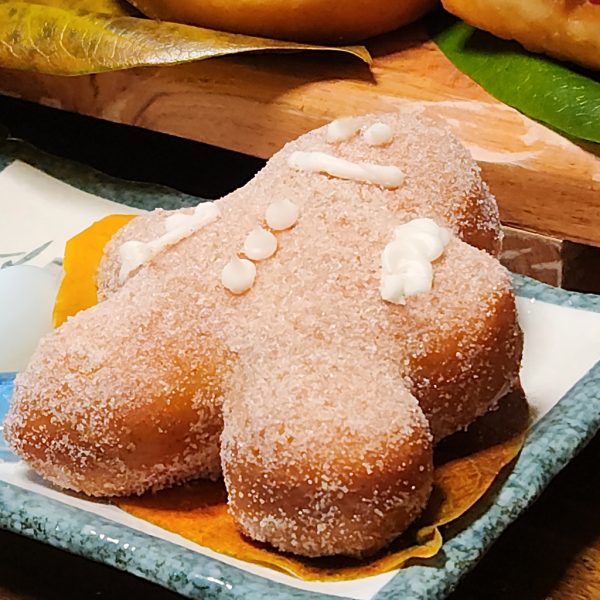 A gingerbread man-shaped donut, coated in sugar glaze, filled with spiced ginger cream cheese, and decorated with icing details, perfect for Christmas celebrations.