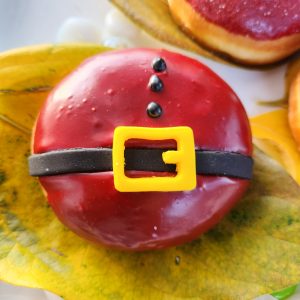 A round Christmas donut with red icing, decorated with a candy black belt and yellow buckle, resembling Santa Claus's outfit.