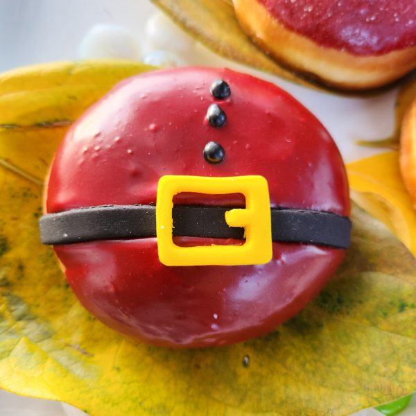 A round Christmas donut with red icing, decorated with a candy black belt and yellow buckle, resembling Santa Claus's outfit.