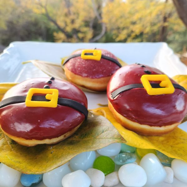 A round Christmas donut with red icing, decorated with a candy black belt and yellow buckle, resembling Santa Claus's outfit.