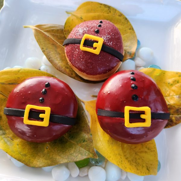 A round Christmas donut with red icing, decorated with a candy black belt and yellow buckle, resembling Santa Claus's outfit.