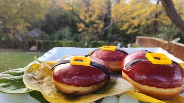 A round Christmas donut with red icing, decorated with a candy black belt and yellow buckle, resembling Santa Claus's outfit.