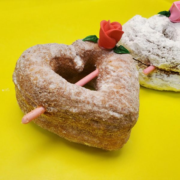 A beautifully crafted Valentine’s Croissant Cupid Heart Donut, dusted with fine sugar, topped with a delicate candy rose, and pierced with a strawberry cream Pocky stick as Cupid’s arrow. A crispy, flaky croissant donut perfect for Valentine’s Day.