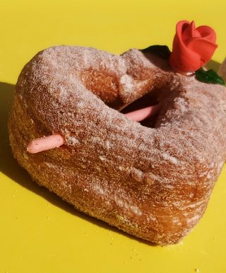 A beautifully crafted Valentine’s Croissant Cupid Heart Donut, dusted with fine sugar, topped with a delicate candy rose, and pierced with a strawberry cream Pocky stick as Cupid’s arrow. A crispy, flaky croissant donut perfect for Valentine’s Day.