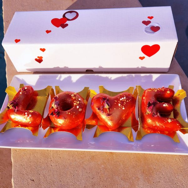 A beautifully arranged Valentine’s LOVE Letter Donut Set with a shiny red mirror glaze, decorated with edible gold flakes and dried rose petals, placed on an elegant gold tray and packaged in a heart-themed Valentine’s gift box. The perfect romantic dessert gift.