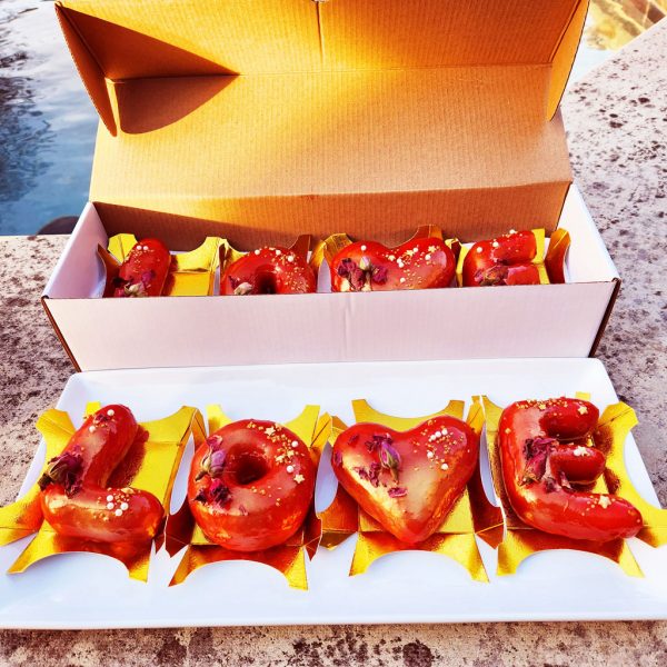 "A beautifully arranged Valentine’s LOVE Letter Donut Set with a shiny red mirror glaze, decorated with edible gold flakes and dried rose petals, placed on an elegant gold tray and packaged in a heart-themed Valentine’s gift box. The perfect romantic dessert gift."