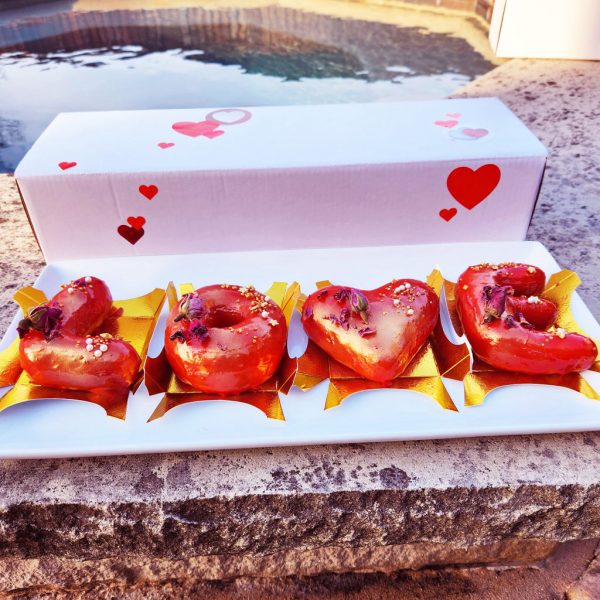 A beautifully arranged LOVE Letter Donut Set with a glossy red mirror glaze, decorated with edible gold flakes and dried rose petals, presented in a luxurious golden tray and Valentine's-themed box.