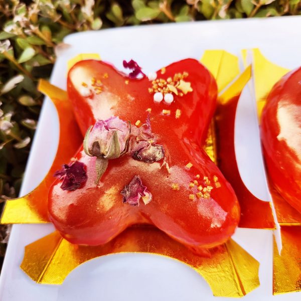 A beautifully crafted Valentine’s XOXO Letter Donut Set, coated in a glossy strawberry mirror glaze, decorated with edible gold flakes and dried rose petals, placed on an elegant gold tray and packaged in a Valentine’s-themed gift box. A sweet and romantic treat for Valentine’s Day.