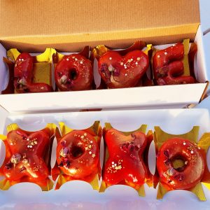 A beautifully crafted Valentine’s XOXO Letter Donut Set, coated in a glossy strawberry mirror glaze, decorated with edible gold flakes and dried rose petals, placed on an elegant gold tray and packaged in a Valentine’s-themed gift box. A sweet and romantic treat for Valentine’s Day.