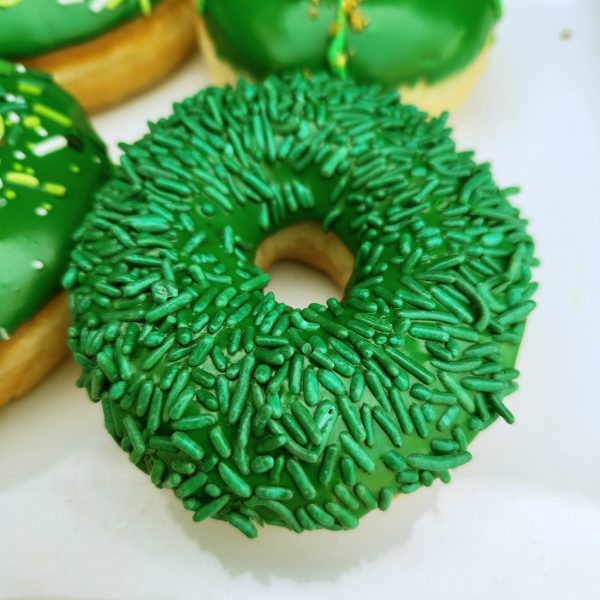 A St. Patrick’s Day-themed donut with green icing and shamrock sprinkles, decorated with a festive mix of green, gold, and white toppings.