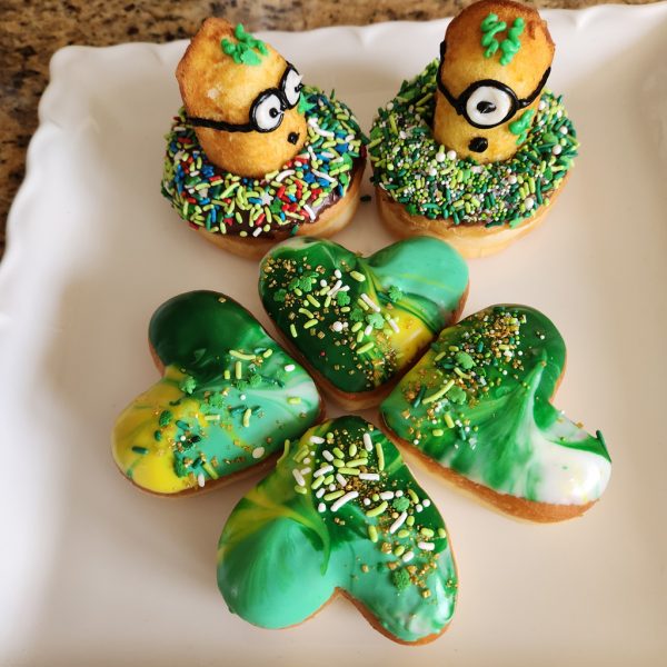 A heart-shaped donut with green, white, and yellow galaxy icing, decorated with festive sprinkles and gold shimmer, perfect for St. Patrick’s Day celebrations.