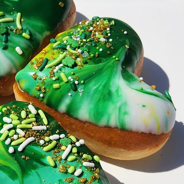 A heart-shaped donut with green, white, and yellow galaxy icing, decorated with festive sprinkles and gold shimmer, perfect for St. Patrick’s Day celebrations.