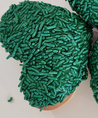 A heart-shaped donut dipped in green icing and completely covered in green sprinkles, making it a festive treat for St. Patrick’s Day.