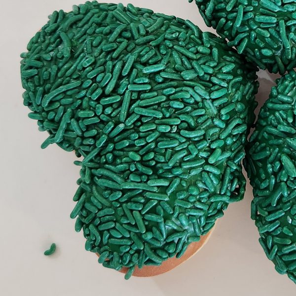 A heart-shaped donut dipped in green icing and completely covered in green sprinkles, making it a festive treat for St. Patrick’s Day.