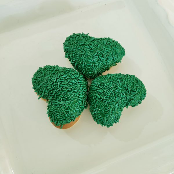 A heart-shaped donut dipped in green icing and completely covered in green sprinkles, making it a festive treat for St. Patrick’s Day.