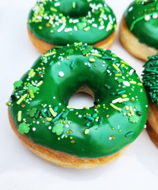 A St. Patrick’s Day-themed donut with green icing and shamrock sprinkles, decorated with a festive mix of green, gold, and white toppings.