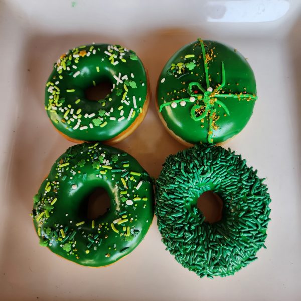 A St. Patrick’s Day-themed donut with green icing and shamrock sprinkles, decorated with a festive mix of green, gold, and white toppings.